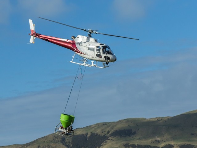 Helicopter with a dropper suspended beneath flies over hills